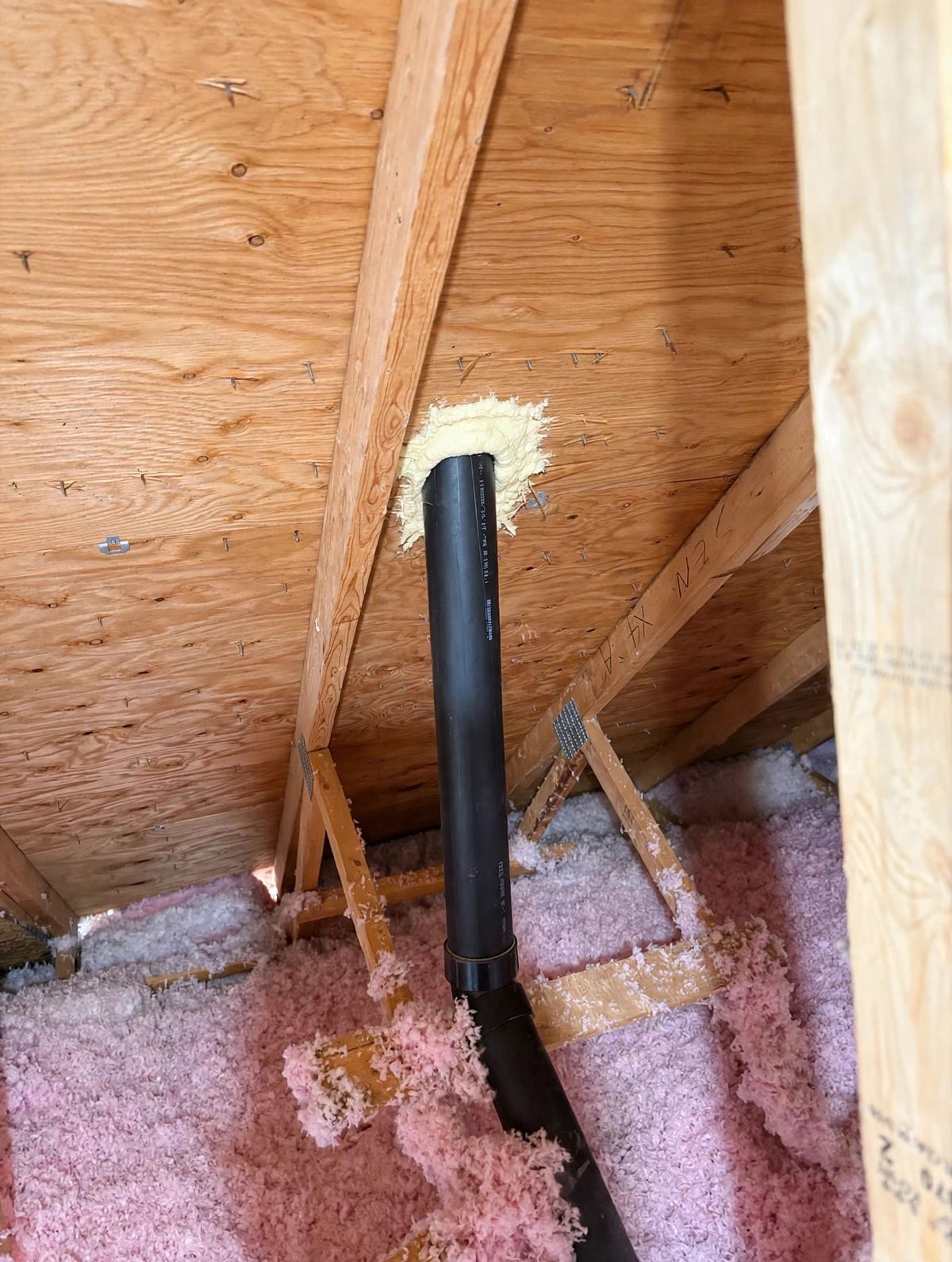 Air-sealed vent pipe with spray foam surrounded by pink insulation