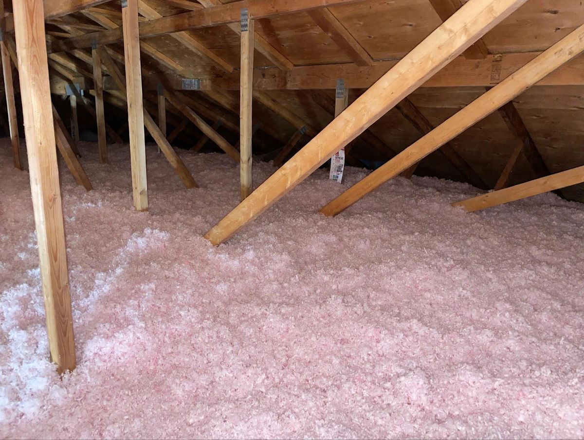 Attic insulation with the R-value certification card attached to a roof truss