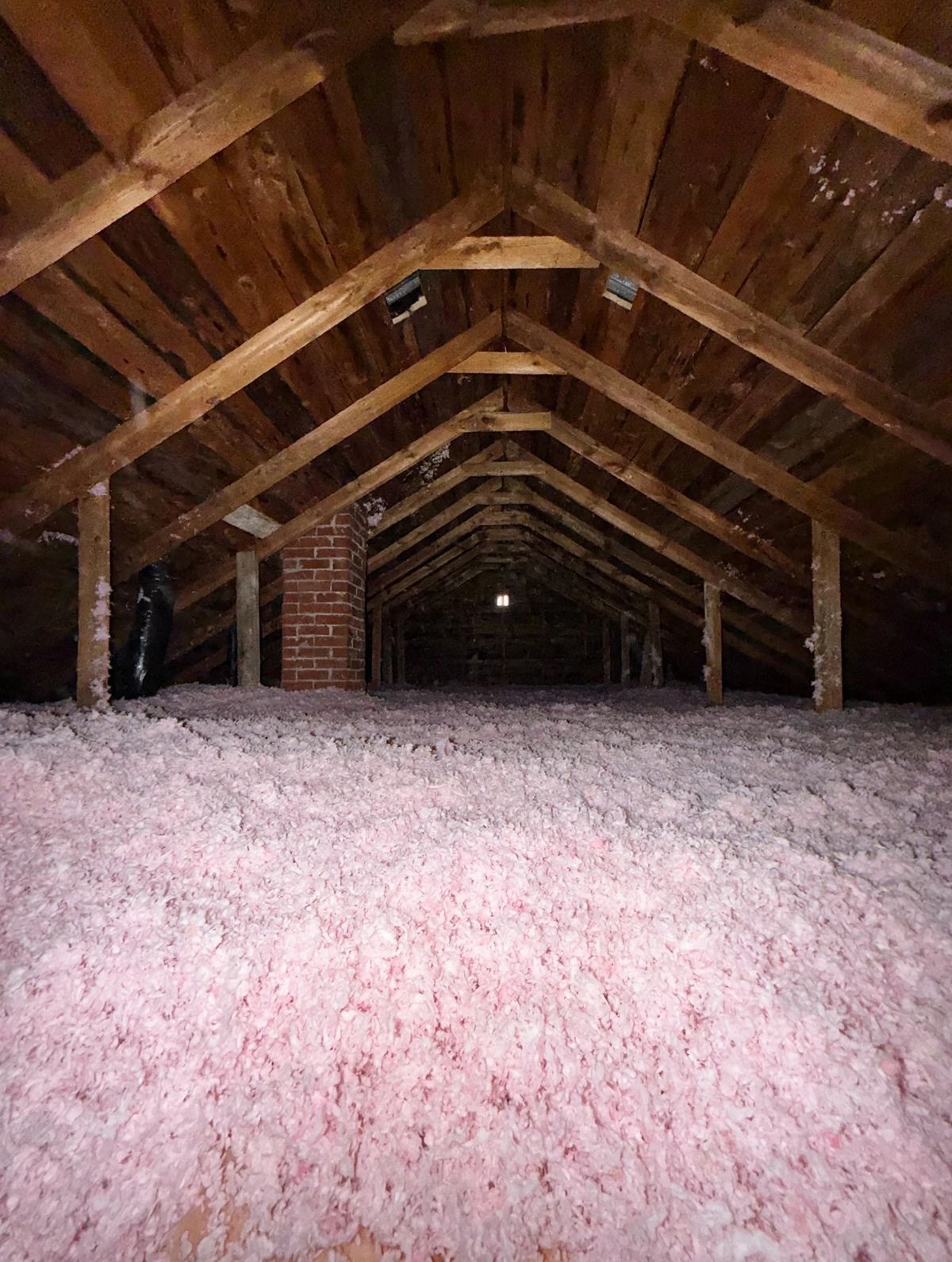Finished attic with deep pink insulation around a brick chimney