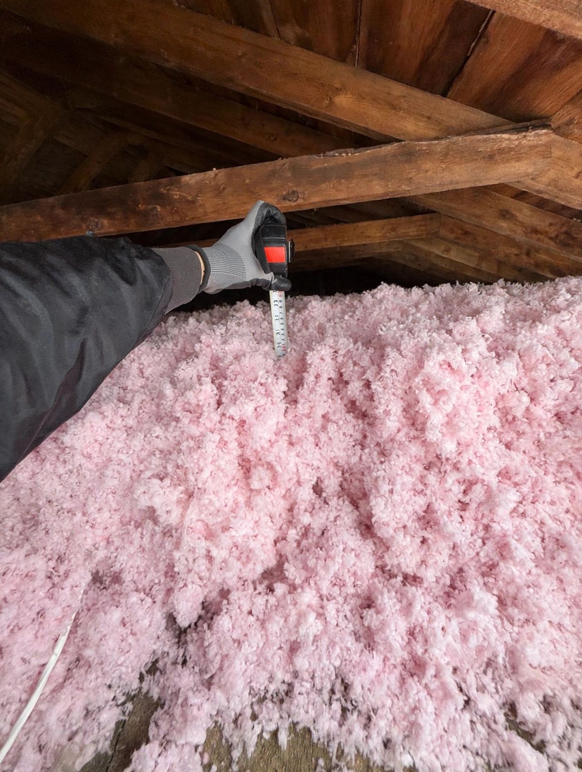 Gloved hand holding a tape measure deep in pink blown-in insulation